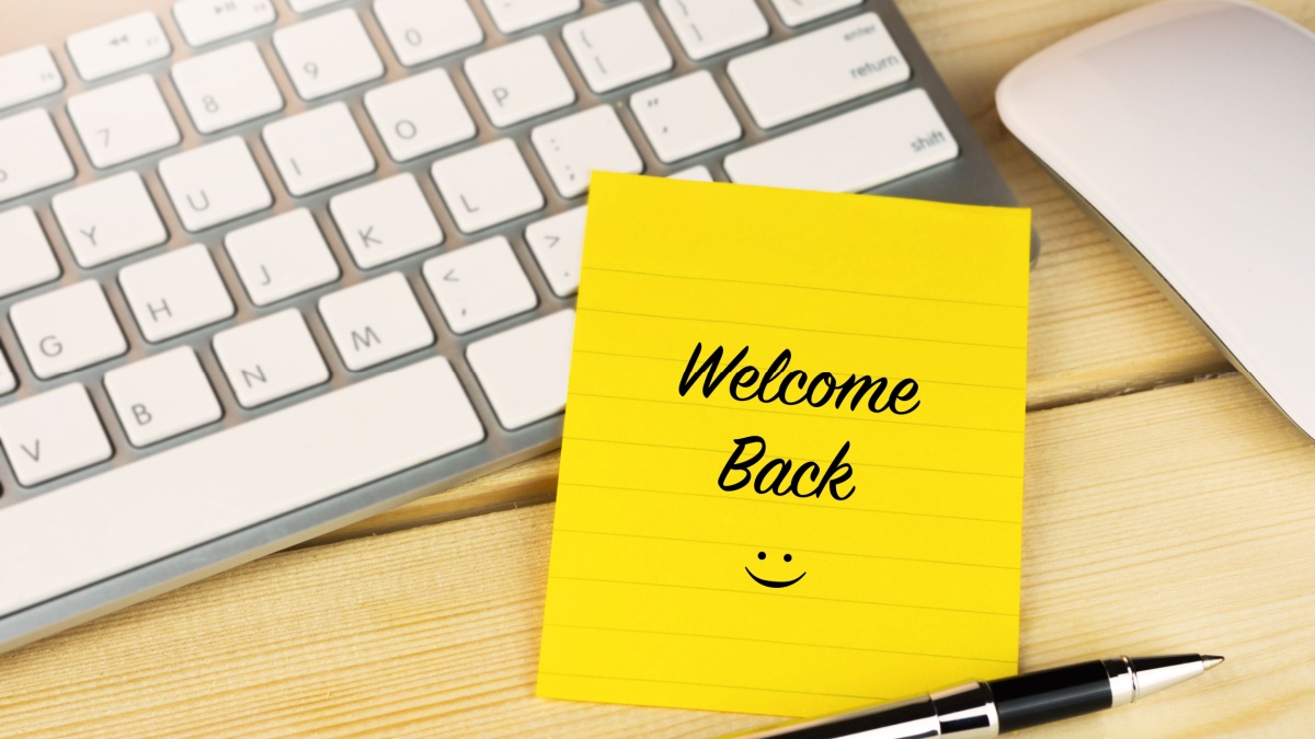 Welcome back is written on a post it note stuck to a keyboard