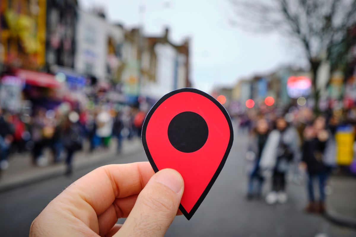 A person holding a geolocation marker with a busy street in the background