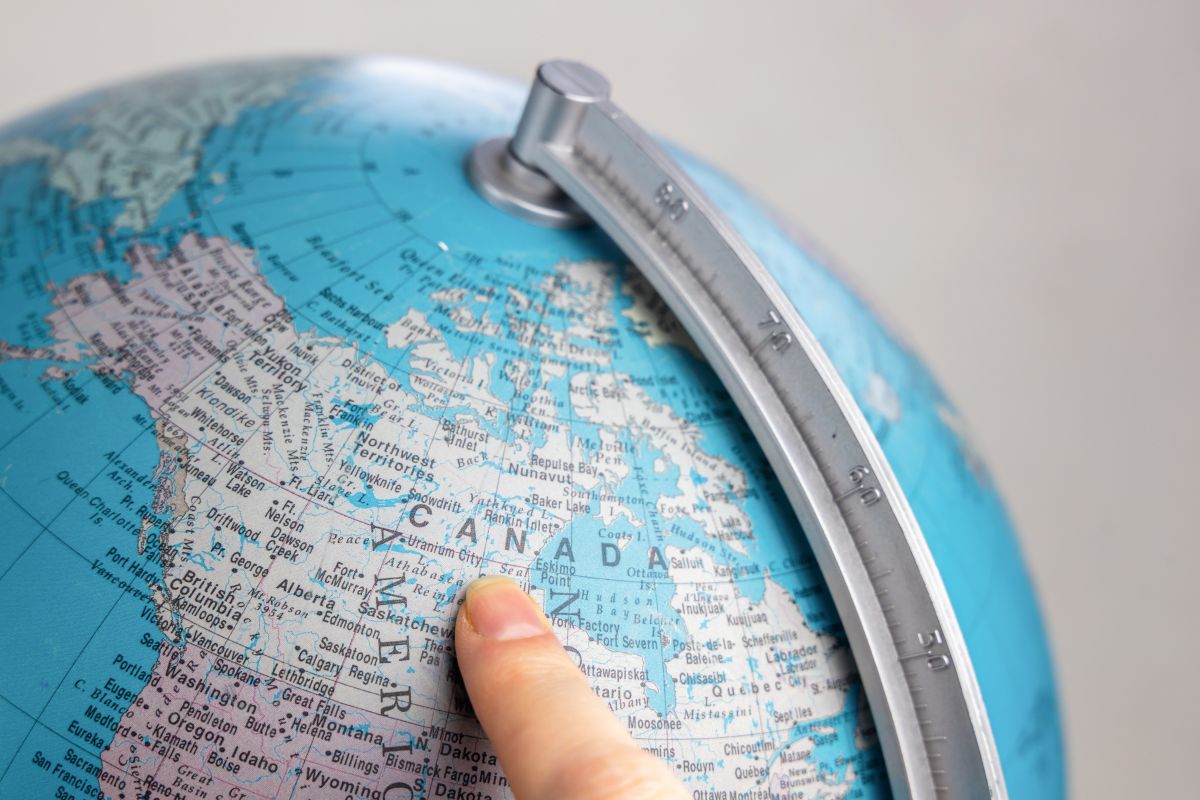 A person pointing at Canada on a globe