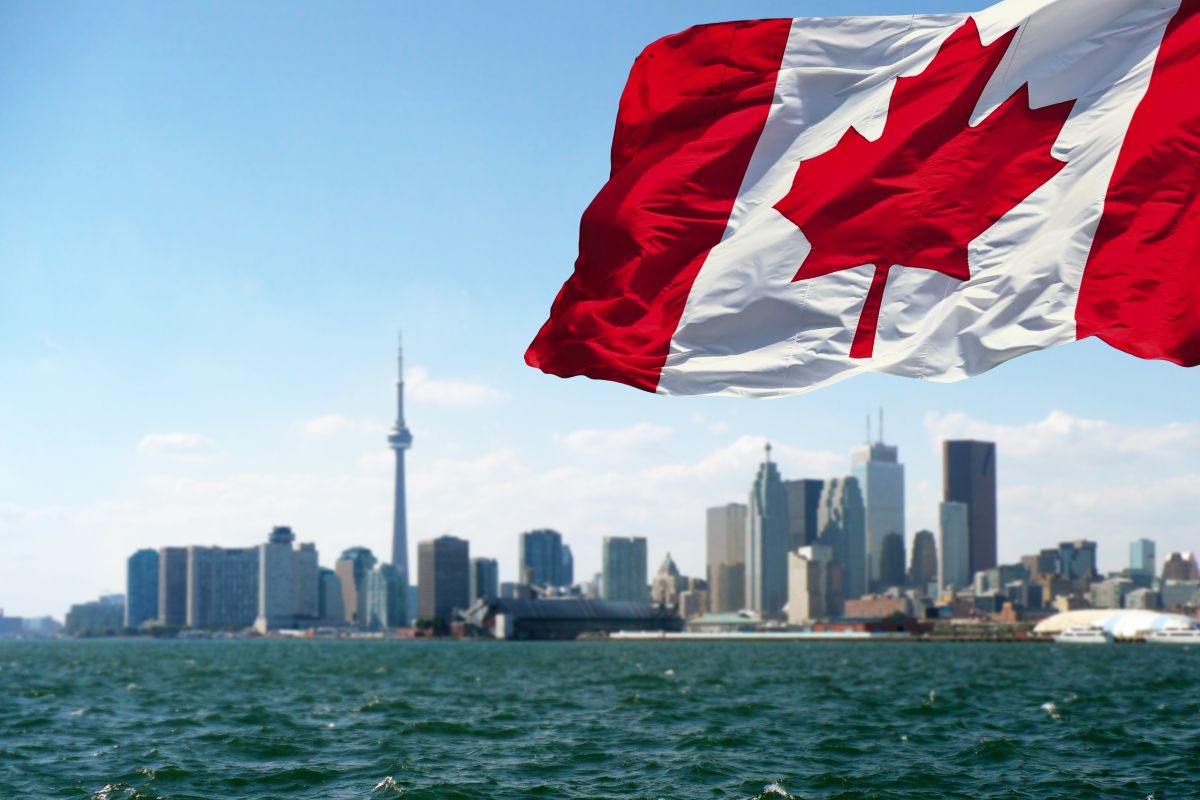 A Canadian flag flying with Lake Ontario and the Toronto skyline in the background