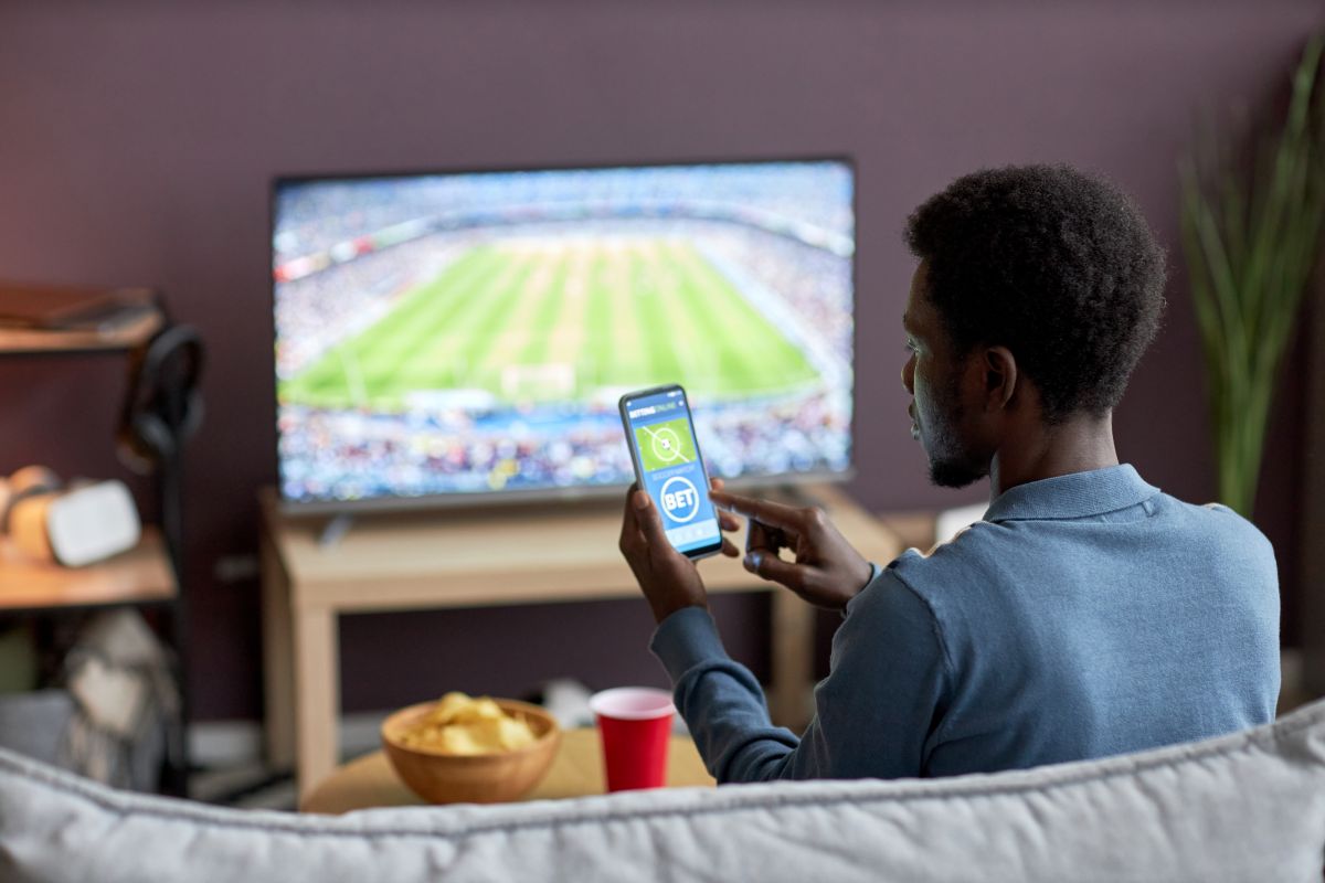 A sports fan watching a game with a betting app open on his phone