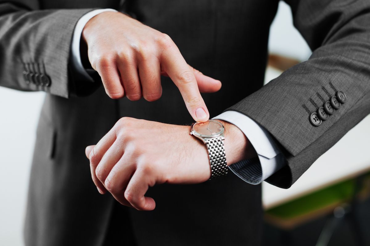 A man points to his wristwatch, displaying the time