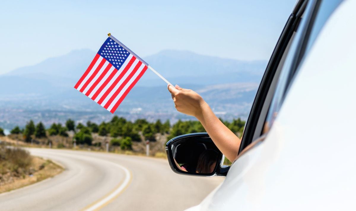 A person waves a USA flag out of a car window
