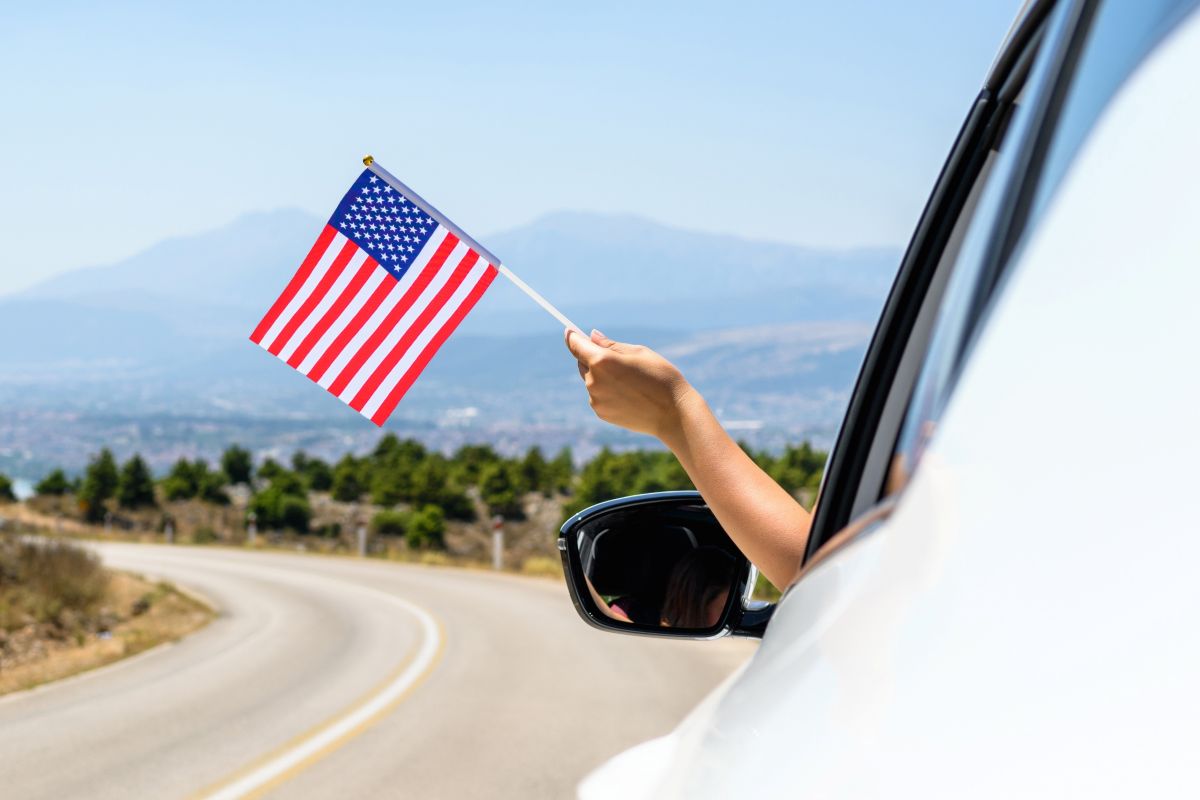 A person waves a USA flag out of a car window