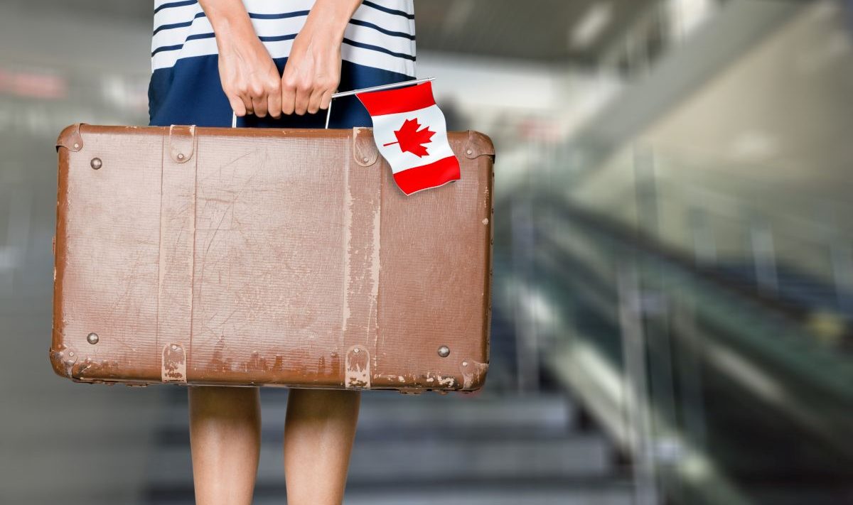 A person carrying a suitcase and holding the Canadian flag