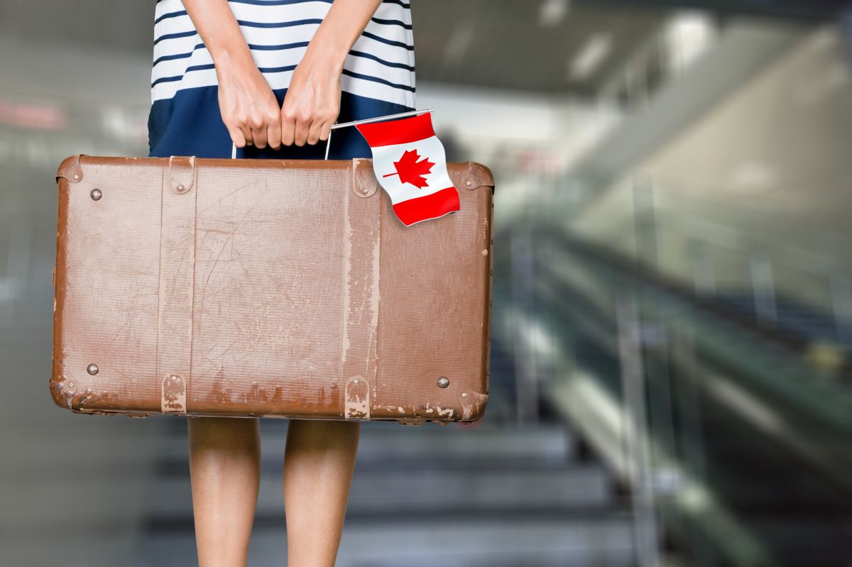 A person carrying a suitcase and holding the Canadian flag
