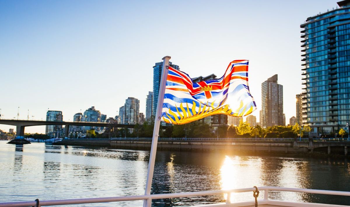 A flag of B.C. on a boat waving in the sunlight with Vancouver in the background