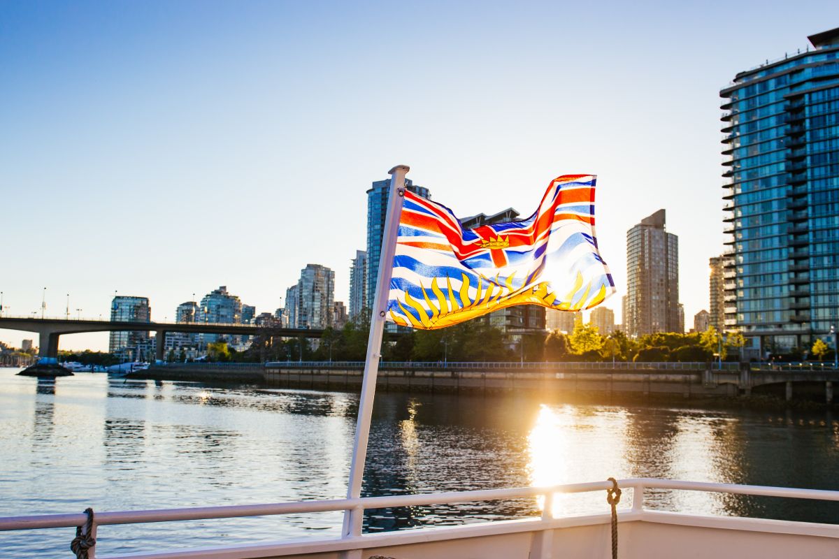 A flag of B.C. on a boat waving in the sunlight with Vancouver in the background