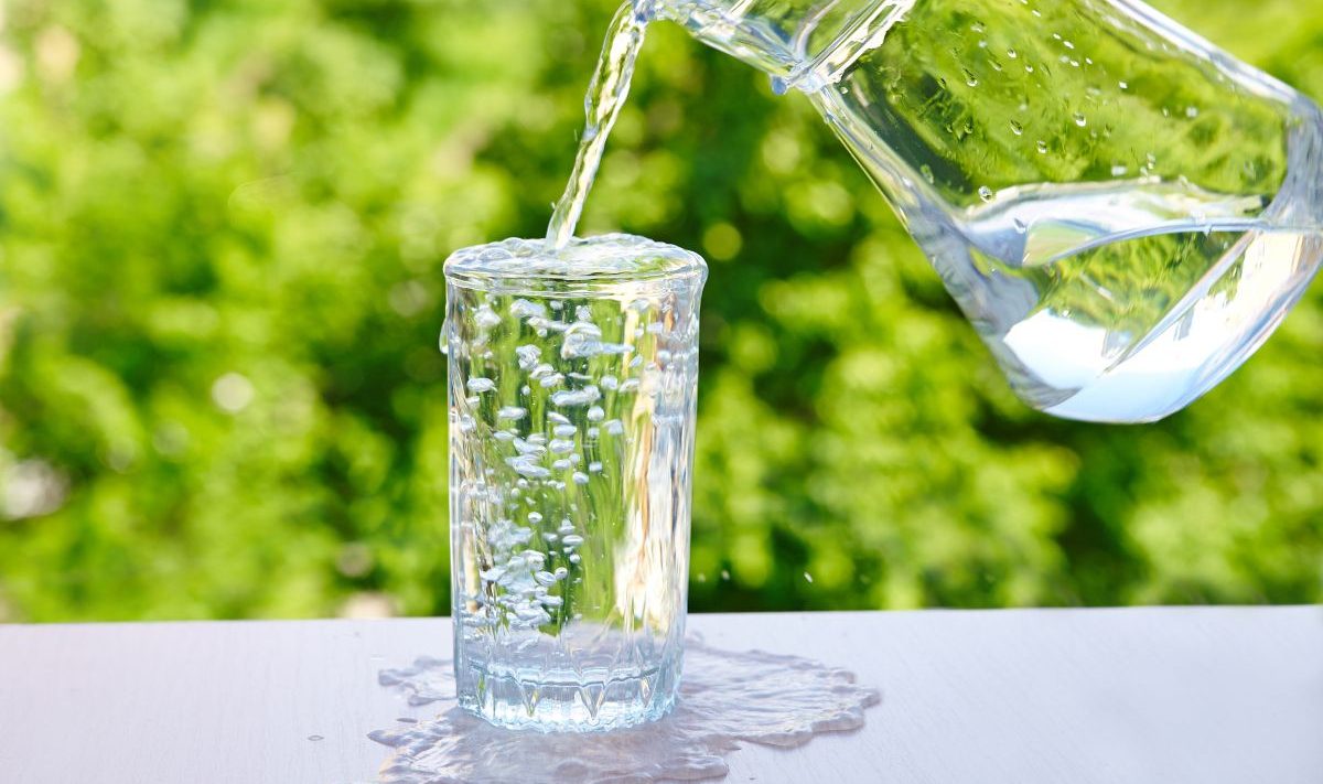 A jug pouring water into a full glass, making it overflow