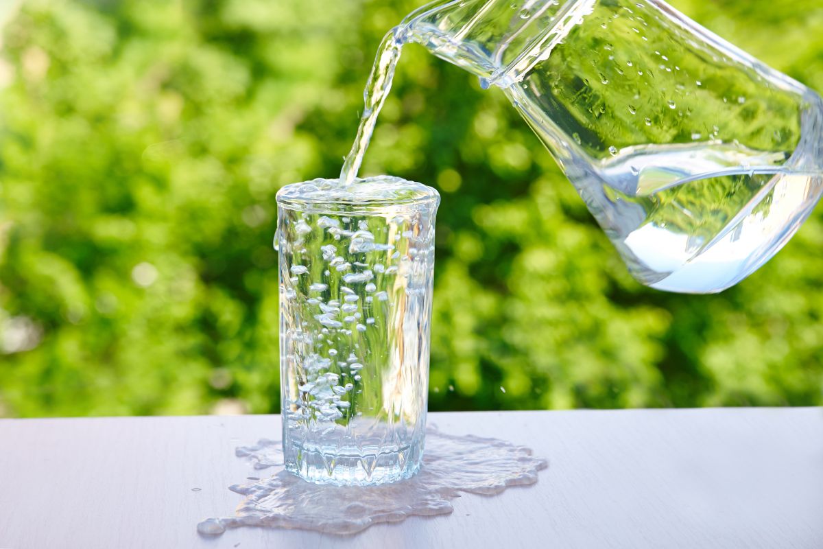 A jug pouring water into a full glass, making it overflow