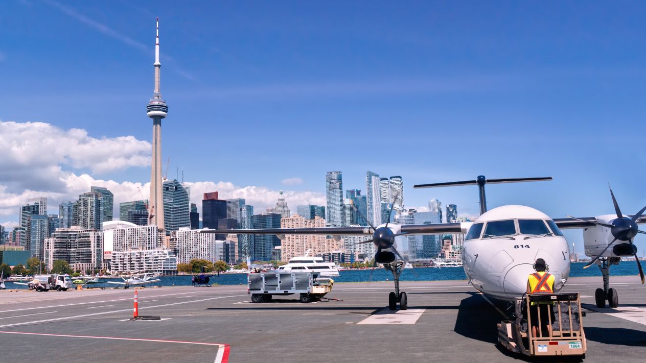A plane waiting on the tarmac at Billy Bishop airport with Toronto's CN Tower in the background